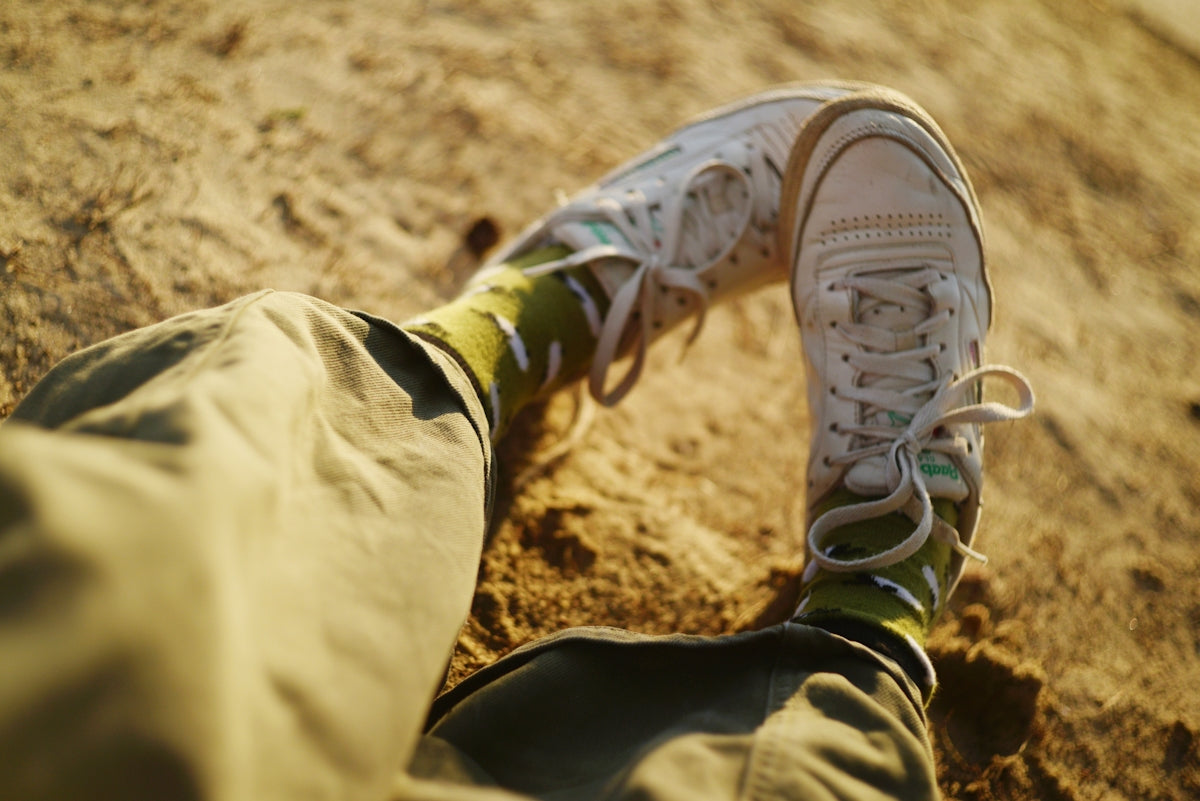 Person sitting on sand with white sneakers and green socks.